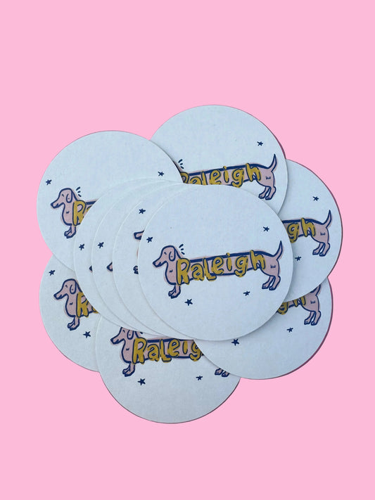 Set of coasters with 'Raleigh' design on a pink surface